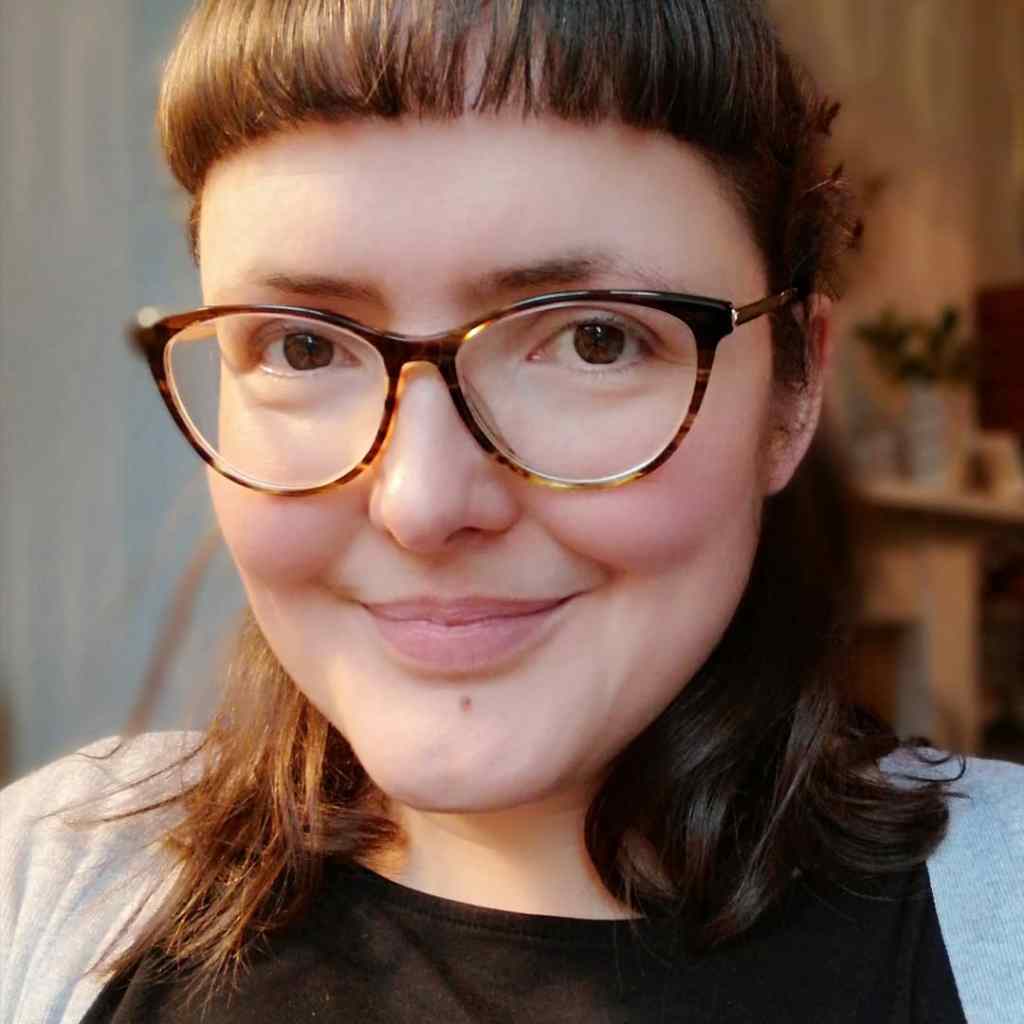 A selfie of Laura's face - smiling. She has dark brown hair, shoulder length with a short fringe. She has pale skin, brown eyes and wears dark-rimmed glasses. She is in her late thirties but does look considerably younger - ha ha!