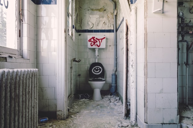 A toilet in a state of disrepair, with graffiti on the lid and cistern, crumbling walls, etc.