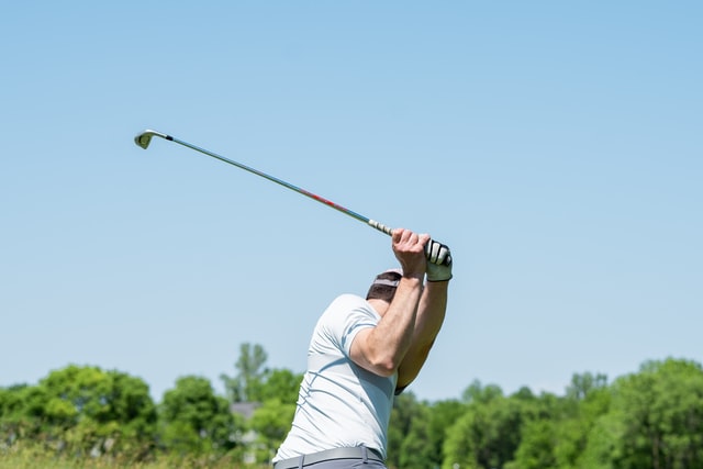 A man mid golf swing under a blue sky.