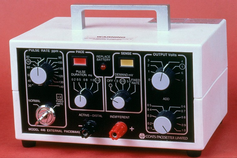 A white box with handle, covered in dials, lights and switches, labelled as (for example) pulse rate, pulse duration, output volts, replace battery, etc.  Company name: Coats Pacesetter Limited.