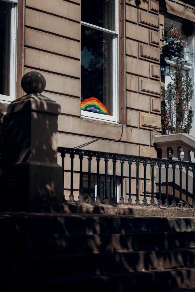 Photograph of a Glasgow tenement building with a rainbow (possibly made of Lego) displayed prominently in a window.