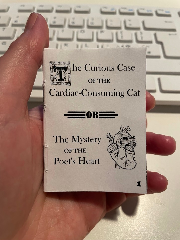 Hand holding a tiny book printed in black and white with cover showing.  Cover: Title page with fancy first letter and a drawing of a heart with a bite mark. Text: The Curious Case of the Cardiac Consuming Cat or The Mystery of the Poet's Heart